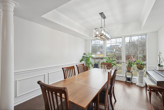 dining space featuring dark wood-type flooring, an inviting chandelier, ornamental molding, a raised ceiling, and ornate columns