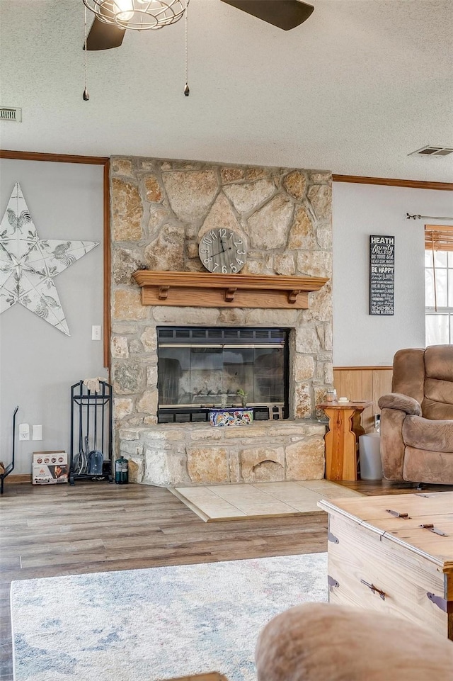 unfurnished living room with a stone fireplace, hardwood / wood-style flooring, ornamental molding, ceiling fan, and a textured ceiling