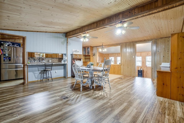 dining room with lofted ceiling with beams, wood walls, ceiling fan, and light wood-type flooring