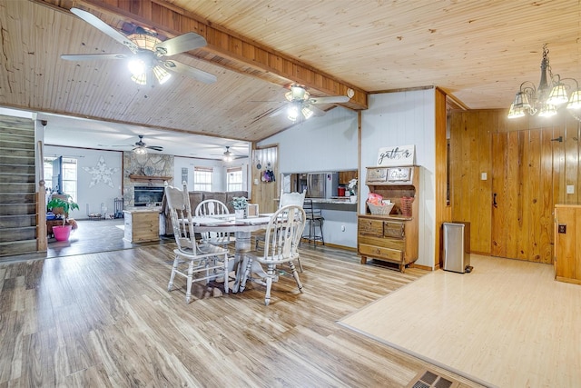 dining space with vaulted ceiling with beams, wood ceiling, a stone fireplace, and light wood-type flooring