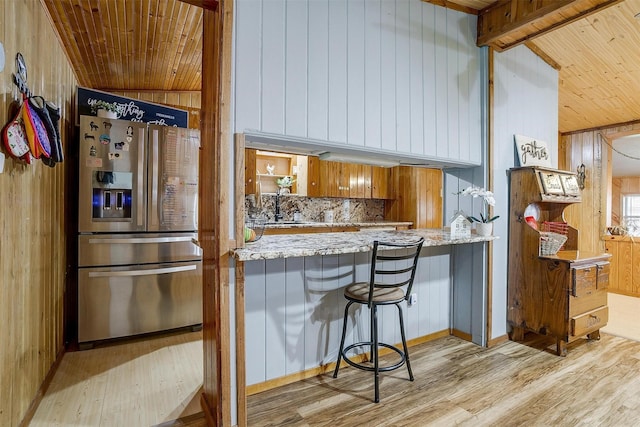 kitchen featuring a kitchen bar, wood walls, stainless steel fridge with ice dispenser, light wood-type flooring, and kitchen peninsula