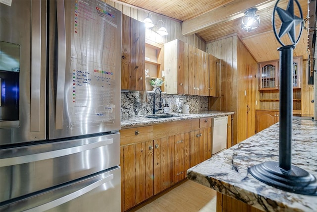 kitchen featuring dishwasher, sink, decorative backsplash, stainless steel refrigerator with ice dispenser, and light stone countertops