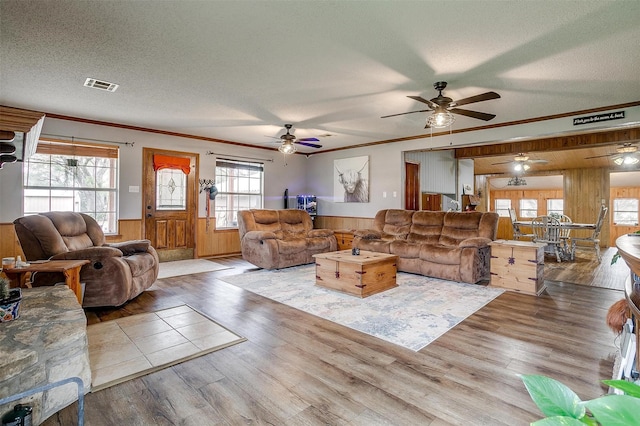 living room with ornamental molding, light hardwood / wood-style floors, a textured ceiling, and wood walls