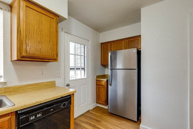 kitchen with dishwasher, sink, stainless steel fridge, and light hardwood / wood-style flooring