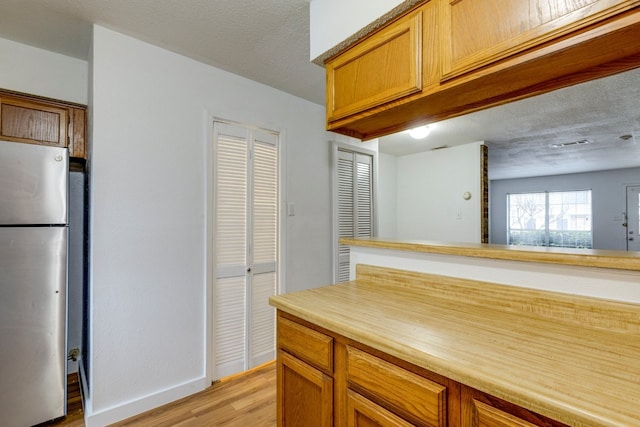 kitchen featuring a textured ceiling, stainless steel fridge, and light hardwood / wood-style floors