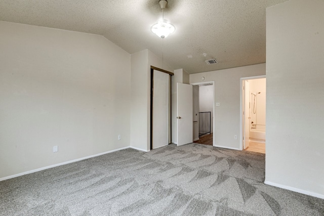 unfurnished bedroom featuring ensuite bathroom, vaulted ceiling, light carpet, and a textured ceiling