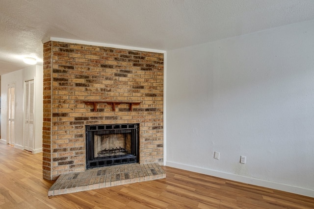 unfurnished living room with a fireplace, a textured ceiling, and light wood-type flooring