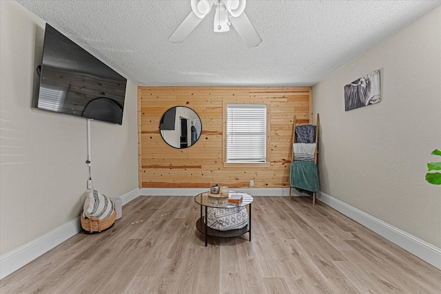 unfurnished room featuring ceiling fan, wooden walls, a textured ceiling, and light wood-type flooring