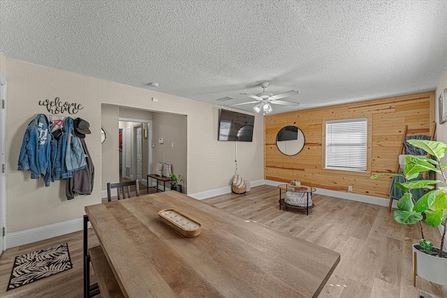 dining space with ceiling fan, light hardwood / wood-style floors, a textured ceiling, and wood walls