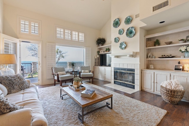 living room featuring a tiled fireplace, built in features, dark wood-type flooring, and high vaulted ceiling