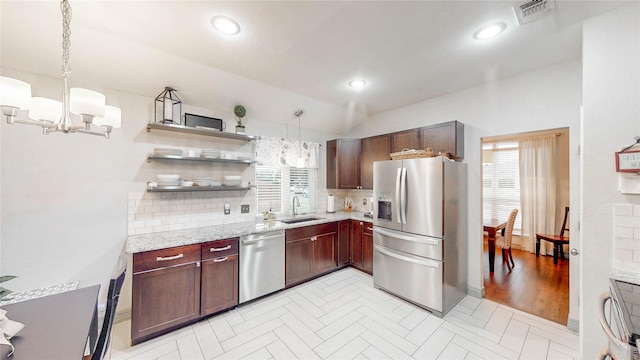 kitchen featuring appliances with stainless steel finishes, hanging light fixtures, light stone counters, a notable chandelier, and decorative backsplash