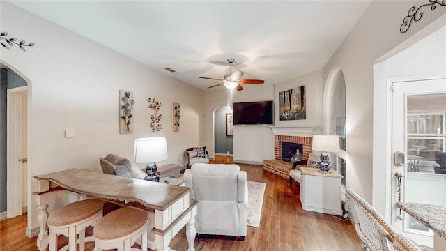 living room featuring hardwood / wood-style flooring, a brick fireplace, and ceiling fan