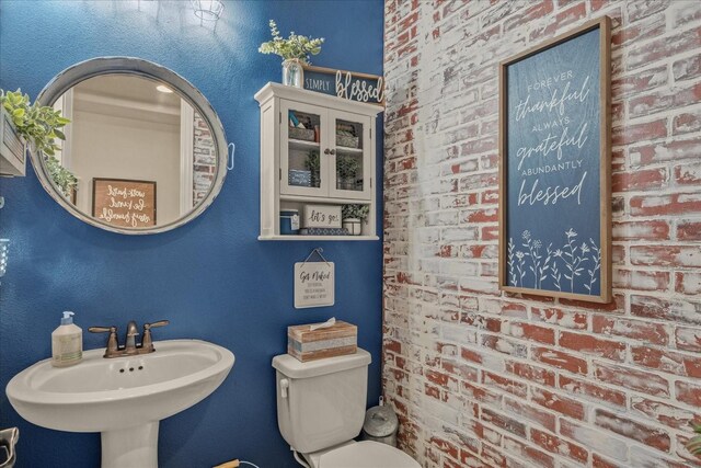 bathroom with brick wall, sink, and toilet