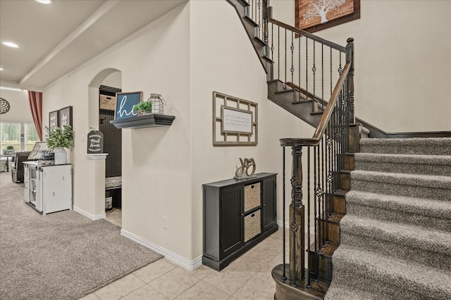 stairway featuring tile patterned flooring, baseboards, carpet, recessed lighting, and arched walkways