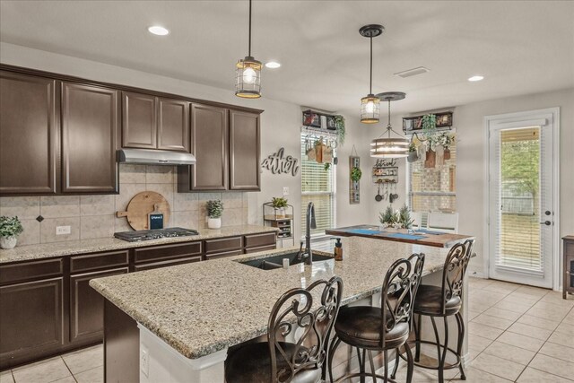 kitchen featuring an island with sink, stainless steel gas stovetop, sink, and hanging light fixtures