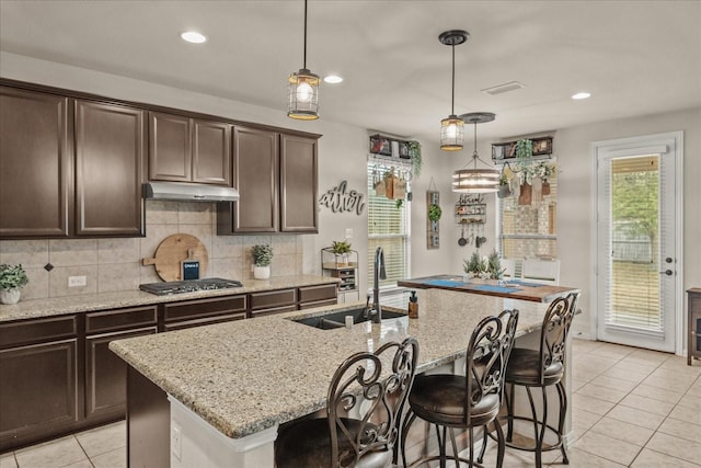 kitchen with a sink, under cabinet range hood, tasteful backsplash, dark brown cabinets, and stainless steel gas cooktop