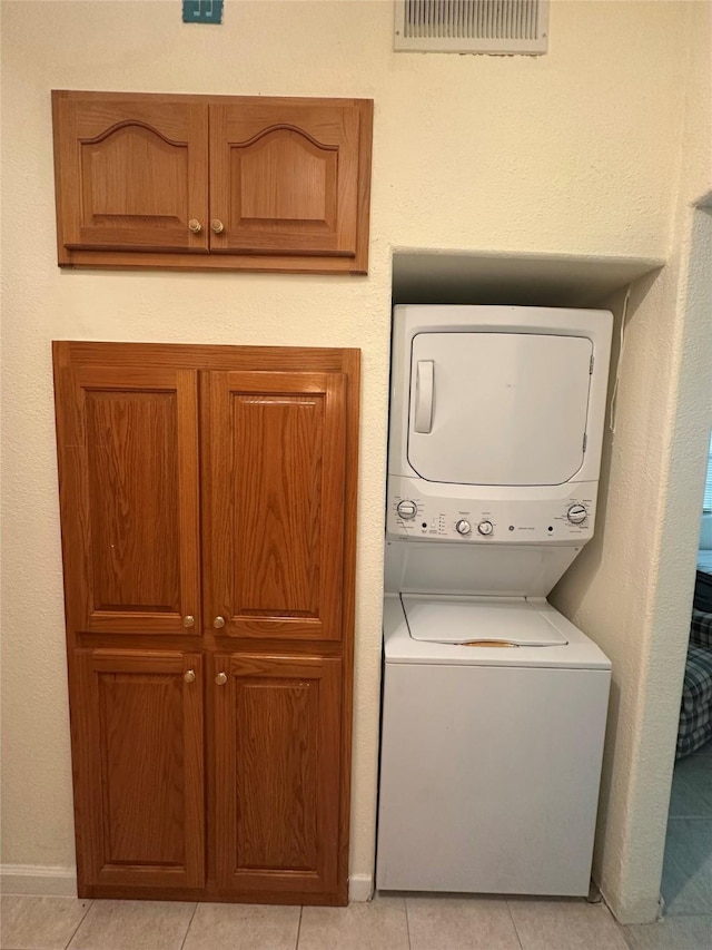 laundry area featuring cabinets, stacked washer / drying machine, and light tile patterned floors