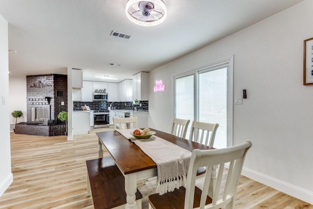 dining room featuring a brick fireplace and light wood-type flooring