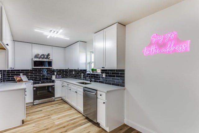 kitchen with light wood-type flooring, a sink, white cabinets, appliances with stainless steel finishes, and tasteful backsplash