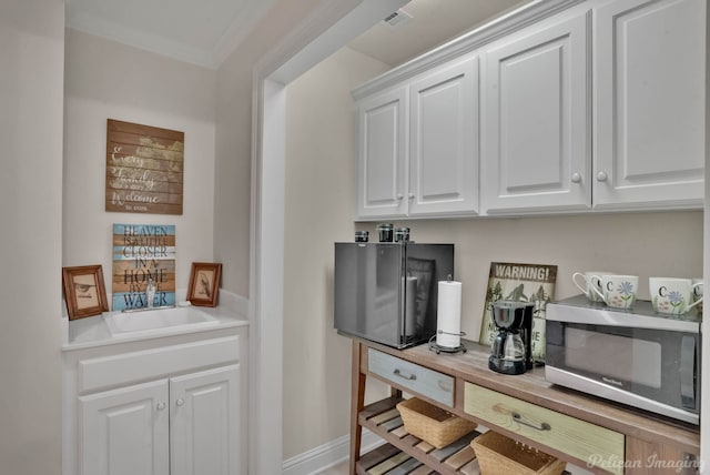 bar with sink, crown molding, and white cabinets