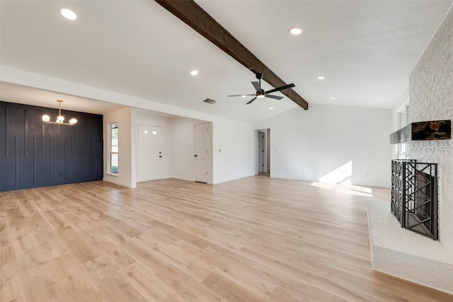 unfurnished living room with lofted ceiling with beams, a brick fireplace, ceiling fan with notable chandelier, and light hardwood / wood-style flooring