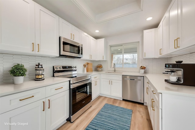 kitchen with appliances with stainless steel finishes, sink, white cabinets, a raised ceiling, and light hardwood / wood-style flooring