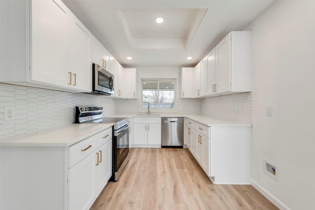 kitchen featuring sink, light wood-type flooring, a raised ceiling, stainless steel appliances, and white cabinets