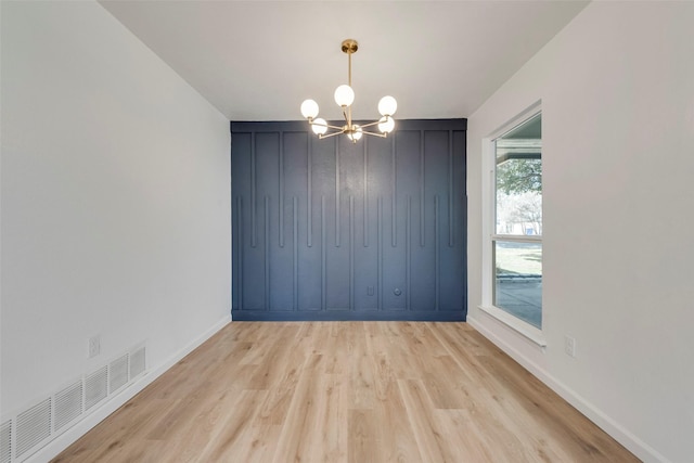 spare room featuring an inviting chandelier and light wood-type flooring