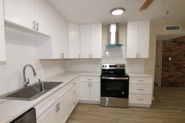 kitchen with sink, white cabinetry, stainless steel appliances, light hardwood / wood-style floors, and wall chimney range hood