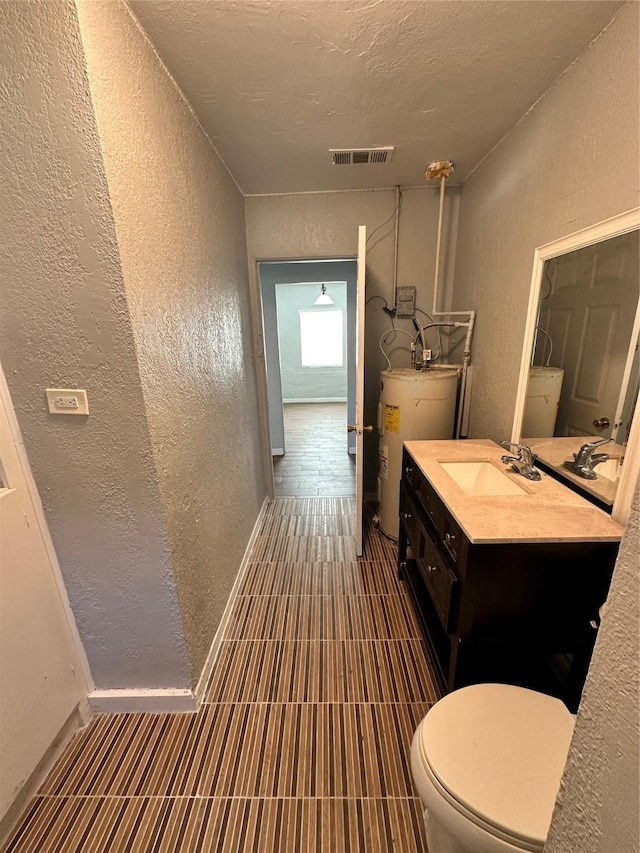 bathroom with vanity, a textured ceiling, water heater, and toilet