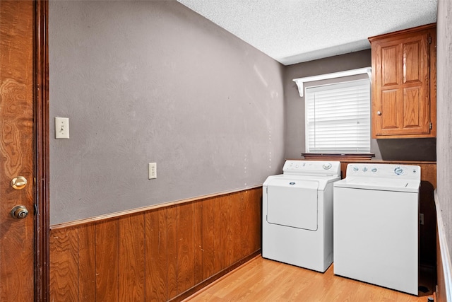 washroom featuring independent washer and dryer, cabinets, light hardwood / wood-style floors, a textured ceiling, and wood walls