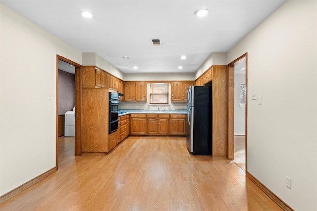 kitchen featuring sink, stainless steel refrigerator, double oven, light hardwood / wood-style floors, and washer / dryer