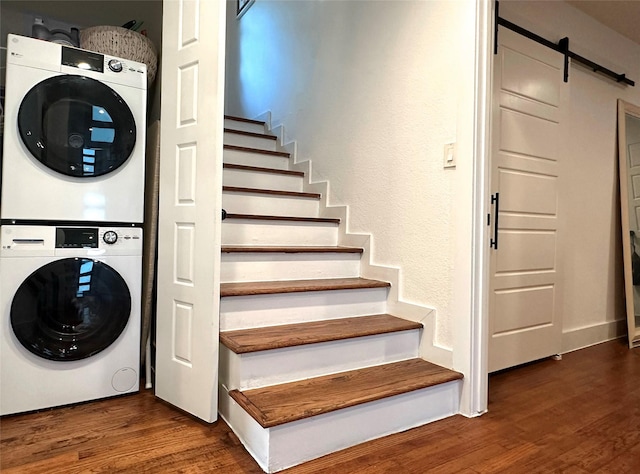 laundry room with laundry area, a barn door, dark wood-style flooring, and stacked washing maching and dryer