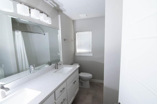 bathroom with double vanity, a sink, toilet, and wood finished floors