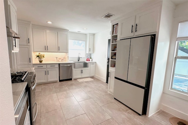 kitchen with stainless steel appliances, light countertops, white cabinetry, a sink, and under cabinet range hood