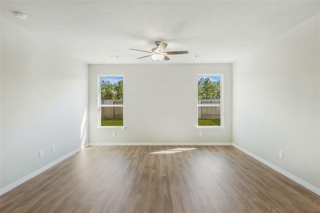 unfurnished room with a ceiling fan, visible vents, baseboards, and wood finished floors