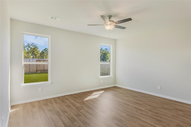 unfurnished room with baseboards, wood finished floors, visible vents, and a healthy amount of sunlight