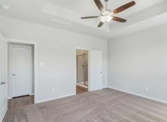 unfurnished bedroom featuring ceiling fan, a tray ceiling, ensuite bathroom, and baseboards