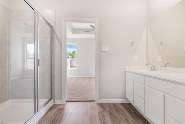 bathroom with double vanity, a stall shower, a sink, wood finished floors, and baseboards