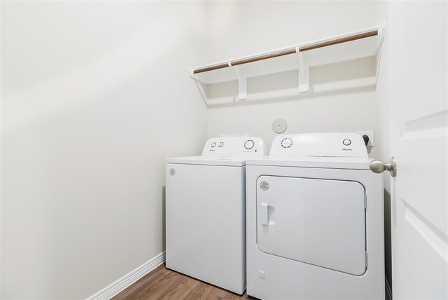 clothes washing area with laundry area, baseboards, washer and dryer, and wood finished floors