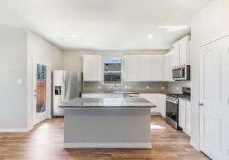 kitchen featuring stainless steel appliances, white cabinetry, a kitchen island, and backsplash