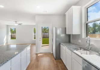 kitchen featuring stainless steel appliances, white cabinetry, a sink, light stone countertops, and light wood-type flooring