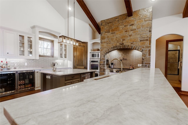 kitchen featuring wine cooler, white cabinetry, pendant lighting, light stone countertops, and a kitchen island with sink