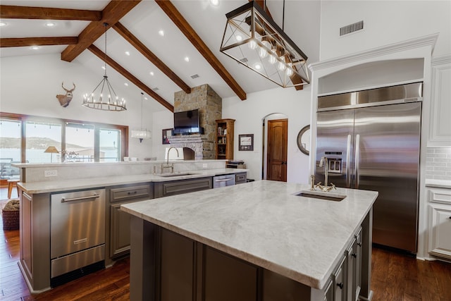 kitchen with sink, dark wood-type flooring, stainless steel appliances, decorative light fixtures, and a large island with sink