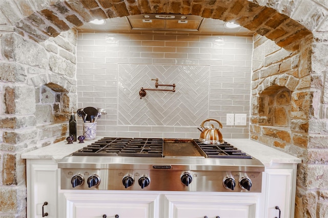 kitchen featuring stainless steel gas stovetop, white cabinetry, light stone countertops, and decorative backsplash