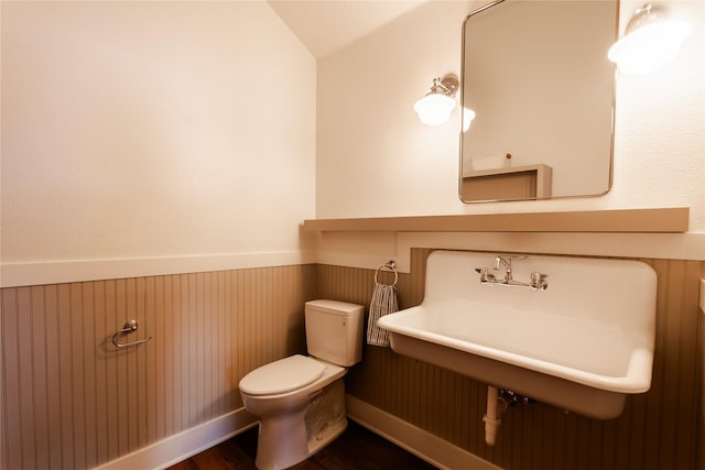 bathroom with toilet, sink, vaulted ceiling, wooden walls, and hardwood / wood-style floors