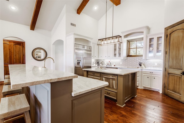 kitchen featuring white cabinetry, stainless steel built in refrigerator, decorative light fixtures, and an island with sink