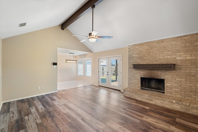 unfurnished living room featuring hardwood / wood-style flooring, ceiling fan, vaulted ceiling with beams, a fireplace, and french doors