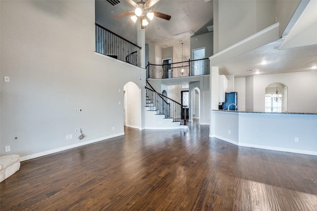 unfurnished living room featuring ceiling fan with notable chandelier, dark hardwood / wood-style floors, and a high ceiling