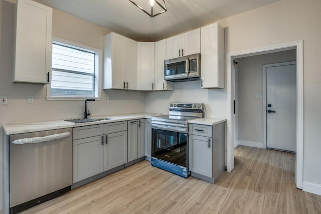 kitchen with sink, gray cabinetry, white cabinets, stainless steel appliances, and light hardwood / wood-style flooring